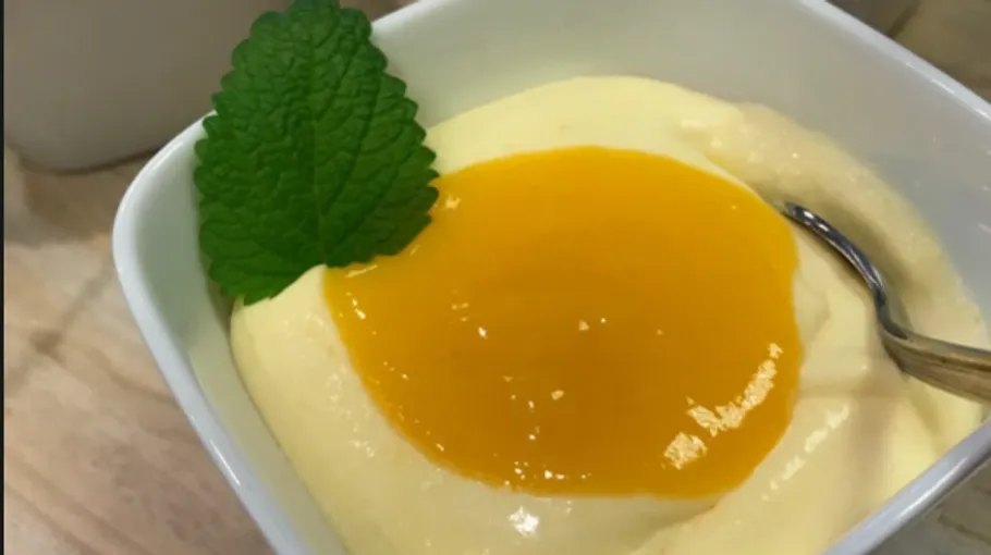 White dessert cup with pudding, apricot sauce and mint.