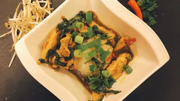 Ein Schüssel Reis mit Gemüse und Hähnchen in Sauce.