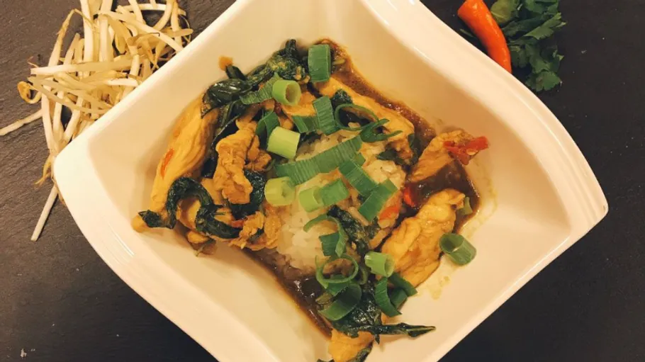 A bowl of rice with vegetables and chicken in sauce.