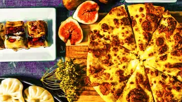 Pizza is on a wooden board surrounded by snacks.