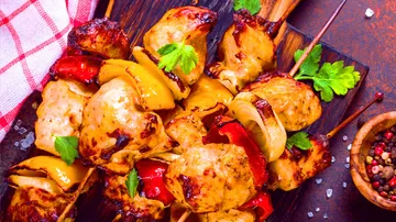 Gegrillte Hähnchenspieße mit buntem Gemüse auf Holzbrett.