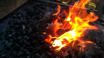 Flame dances over coal-black ground in the open.
