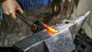 Schmied bearbeitet glühendes Metall auf einem Amboss.