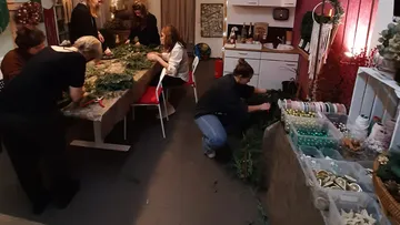 Women make wreaths together in a cozy room.
