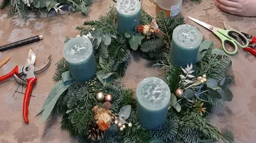 Green candles stand in a decorative Christmas wreath.