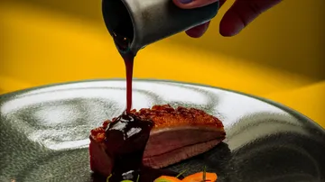 Eine Sauce wird über ein gebratenes Stück Fleisch gegossen.