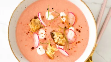 Pink soup decorated with radishes and pieces of bread.