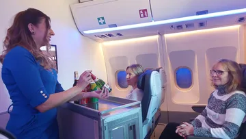 Flugbegleiterin serviert Getränke an Passagiere im Flugzeug.
