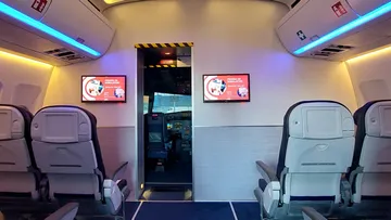 Flughafen-Simulator: Leere Sitze vor Cockpittür mit Bildschirmen.