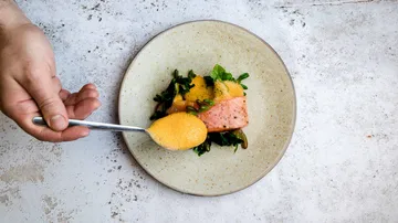 Löffel hebt Creme von einem Teller mit Lachs und Salat.