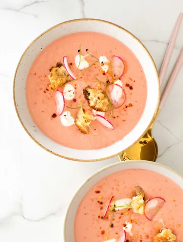 Bowl of pink soup topped with radishes and croutons.