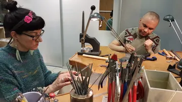 Zwei Menschen arbeiten an einem Tisch mit Werkzeugen.