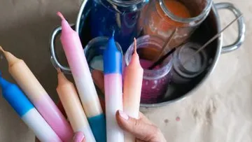 Hand, die bunte Tauchkerzen über Gläsern hält.