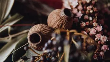 Zwei geflochtene Keramikkugeln liegen zwischen bunten Blumen.