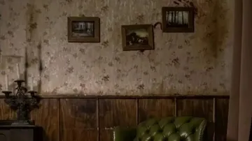 Green sofa stands in front of a flowery wall with pictures.