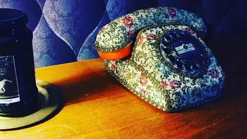 Colourful vintage telephone is lying on a wooden table with glass next to it.