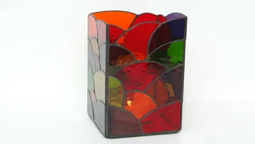 Vase aus buntem Glas steht auf weißem Hintergrund.