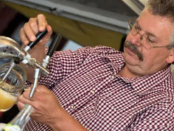 Man taps beer from a glass in a party tent.
