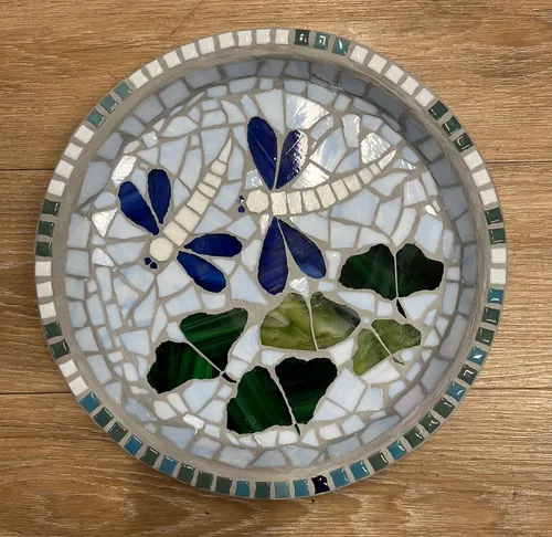 Runde Mosaikplatte mit blauen Schmetterlingen und grünen Blättern.