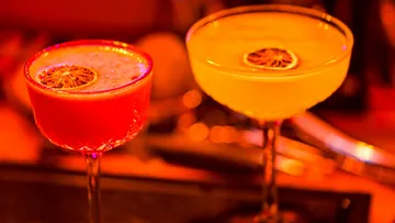 Two cocktails are sitting on a table with dim lighting.