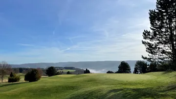 Green hills with trees under clear blue skies.