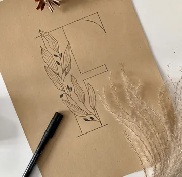 Stift zeichnet einen geschwungenen Buchstaben auf braunem Papier.