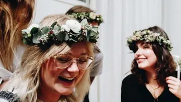 Women with flower wreaths laugh and interact in bright surroundings.