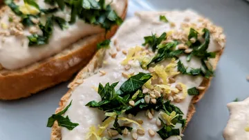 Brot mit cremigem Aufstrich, belegt mit Kräutern und Sesam.