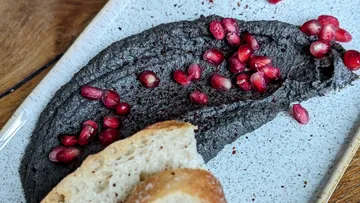 Black dip with pomegranate seeds and bread on plate.