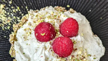 Dessert mit Himbeeren und gehackten Pistazien in Schüssel.