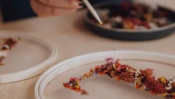 A person arranges dried flowers on a table.