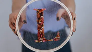 Embroidery frame shows the letter “L” made of floral material.