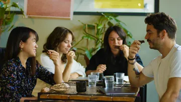 Four people enjoy snacks and laugh in a café.