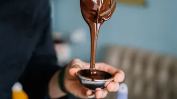 One hand holds liquid chocolate over a small bowl.