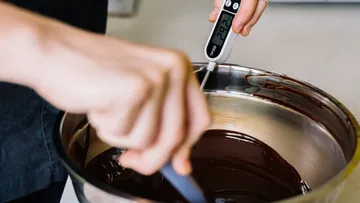 A hand stirs in melted chocolate in a bowl.