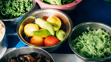 Frische Gemüse und Obst liegen in Schalen auf Tisch.