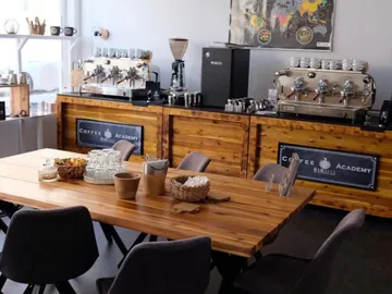 Wooden table with chairs surrounded by coffee facilities and appliances.