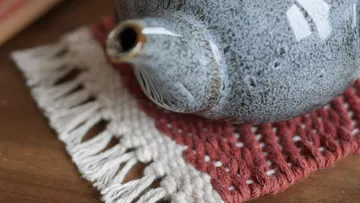 Grey teapot stands on a hand-woven trivet.