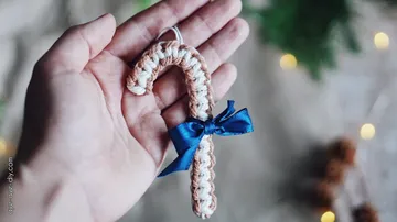 Hand holding a handmade candy cane pendant with bow
