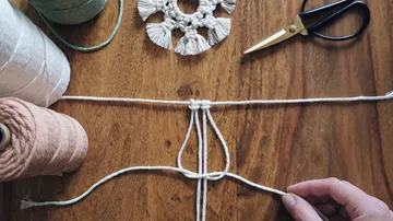 Fäden werden verknüpft, während Handwerk auf Holz-Unterlage liegt.
