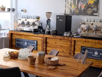 Wooden table with chairs surrounded by café barista equipment.