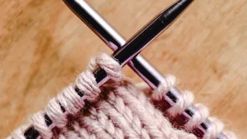 Knitting needles keep pink woolen work on wood surface.