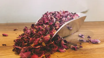 Rosenblütenblätter fallen aus einem silbernen Schaufel auf Holz.