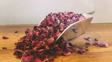 Rose petals lie on a wooden board next to a shovel.