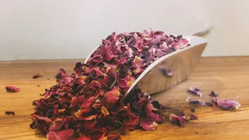 Rosenblätter fallen aus einer edelstahlernen Schaufel auf Holz.