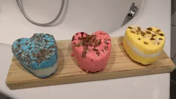 Herzförmige Badebomben liegen auf einem Holzbrett im Bad.