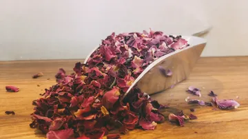 Rose petals fall from a metal shovel onto wood.