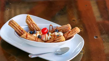 Churros with ice cream and fruit on a white plate.