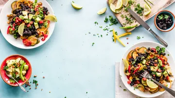 Two colorful salads are lying on a table with herbs.