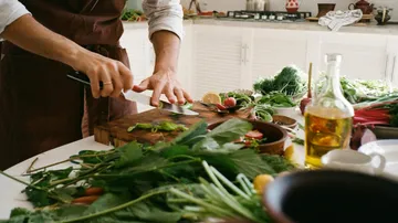 Cook cuts fresh vegetables on a table in the kitchen.